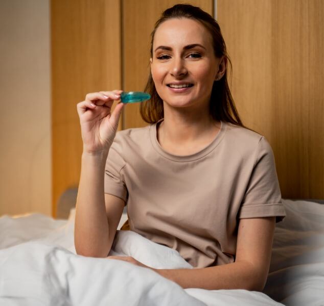 Woman sitting up in bed smiling and holding oral appliance