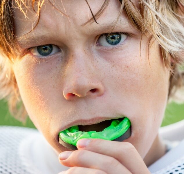 Young boy placing green athletic mouthguard over his teeth