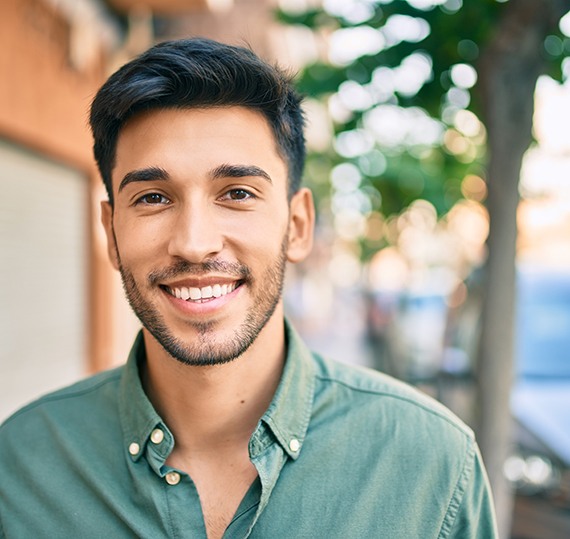 Man in green shirt standing next to house and smiling