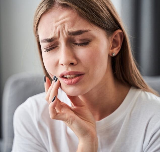 Woman wincing and holding her cheek in pain needing emergency dentist in Springfield