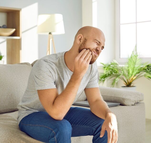 Man wincing and holding his cheek in pain before tooth extractions in Springfield