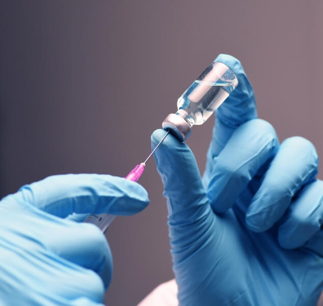 Medical professional drawing syringe from vial of clear liquid