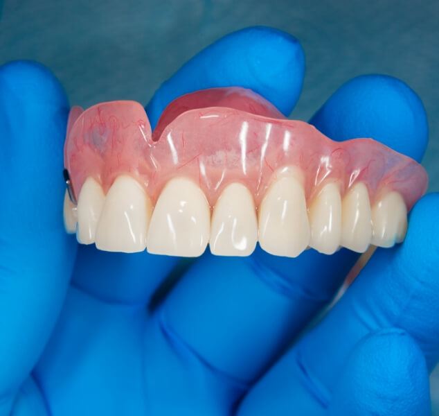 Gloved hand holding a full upper denture