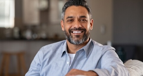 Man in light blue buttoned shirt sitting on couch and smiling