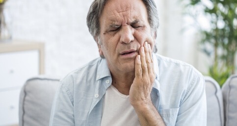 Older man wincing and holding his cheek