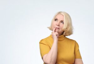 Woman wearing questioning expression, finger on chin, looking upward.